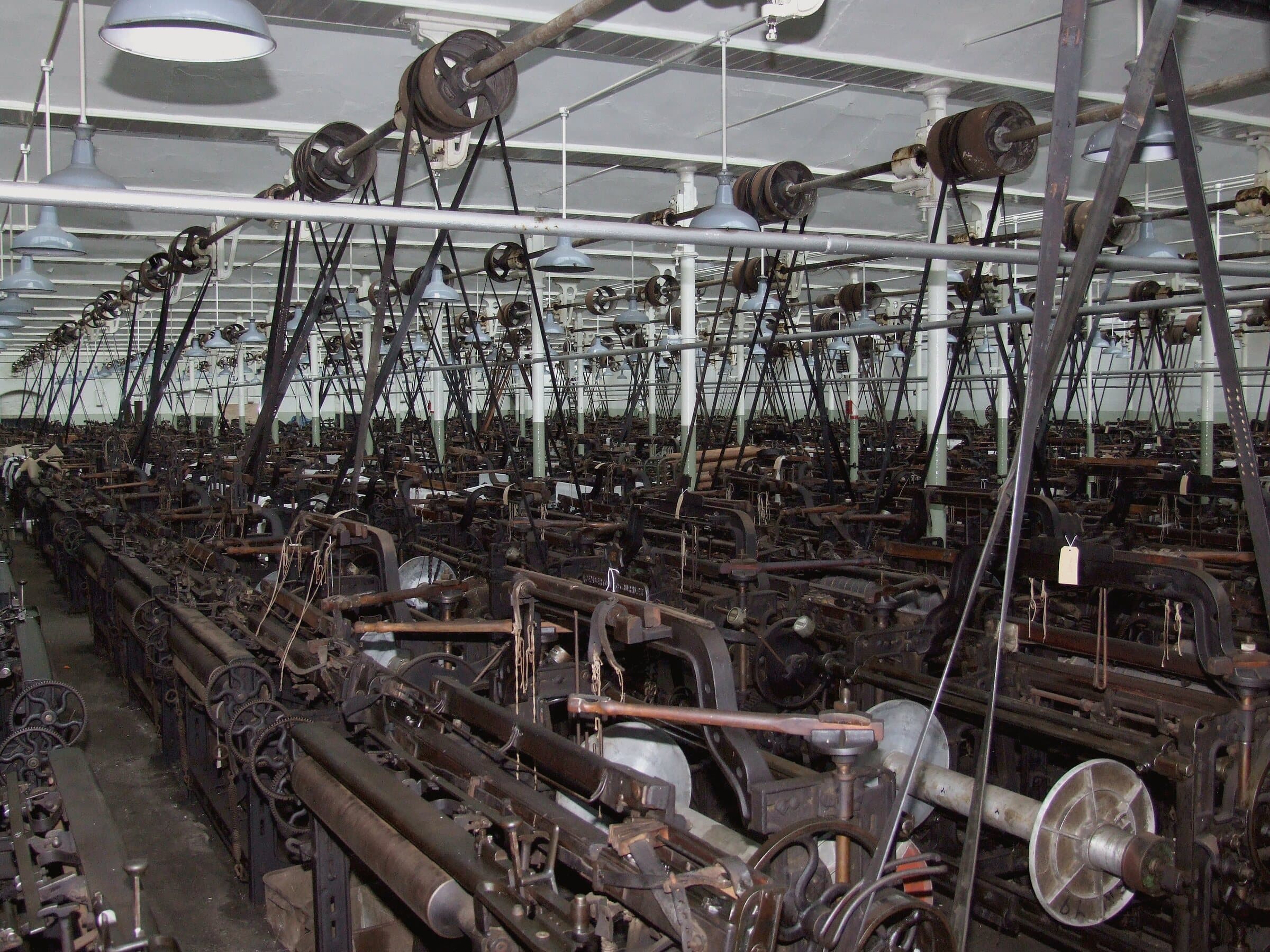 A weaving shed filled with rows of power looms under a north-light roof.