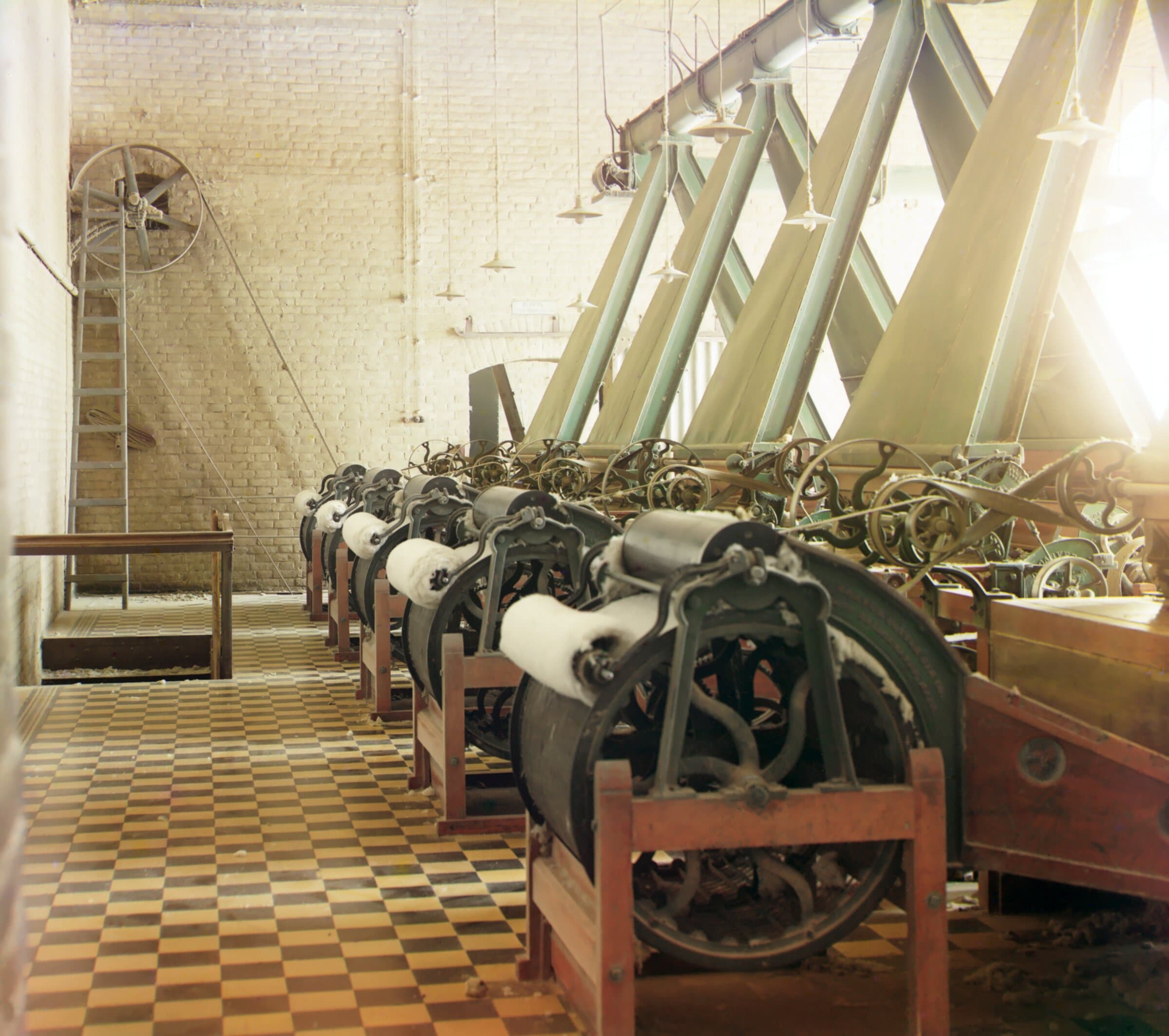 Interior of a cotton textile mill photographed in 1911, sunlight falling across rows of spinning frames on a tiled floor.