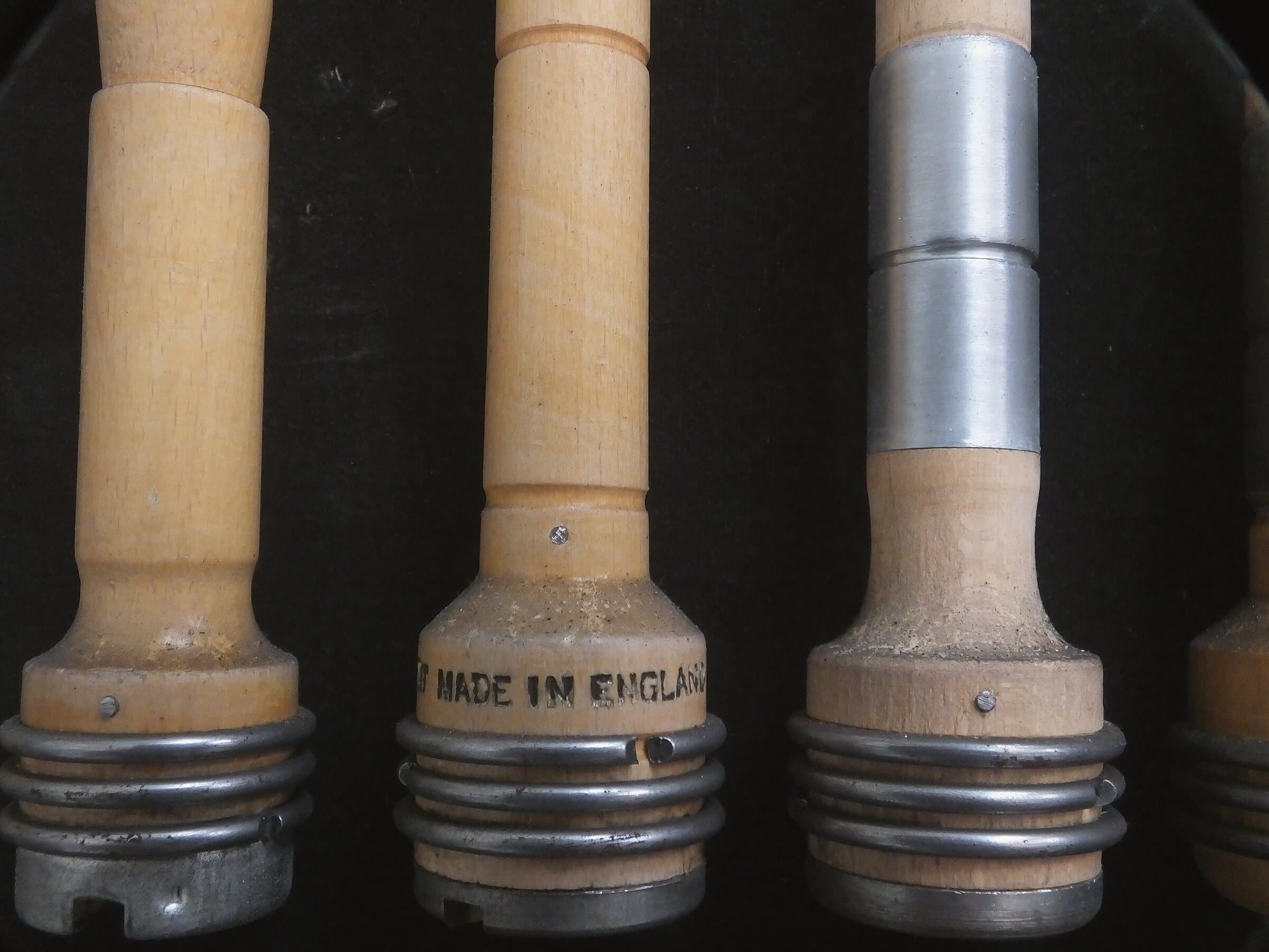 Three turned wooden pirns standing against a dark ground, one stamped Made in England.