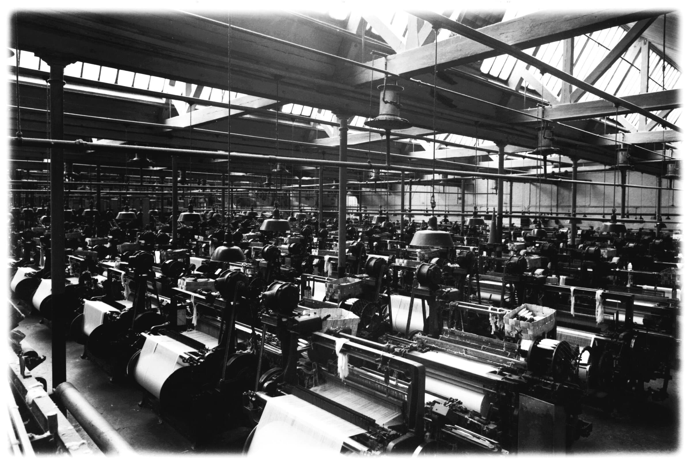 Photograph from 1877 of a vast weaving hall packed with looms under an iron-framed roof.